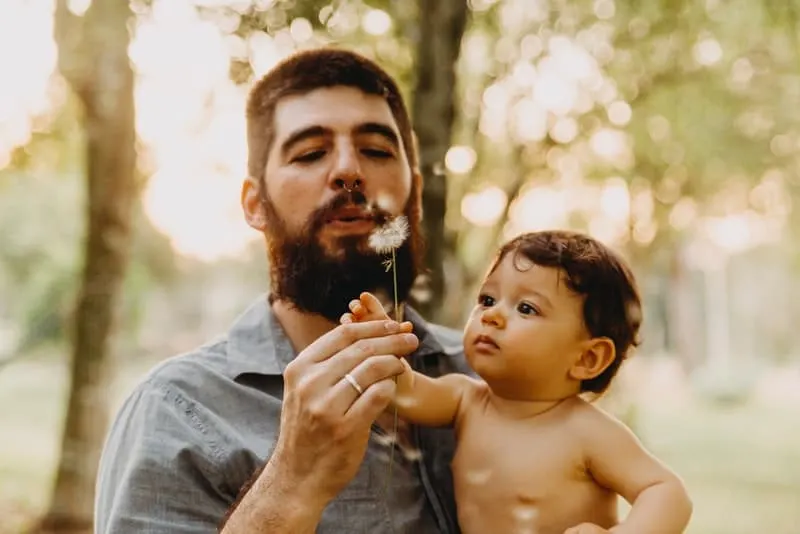 Draußen steht ein Mann mit Bart, der ein Baby in den Armen hält