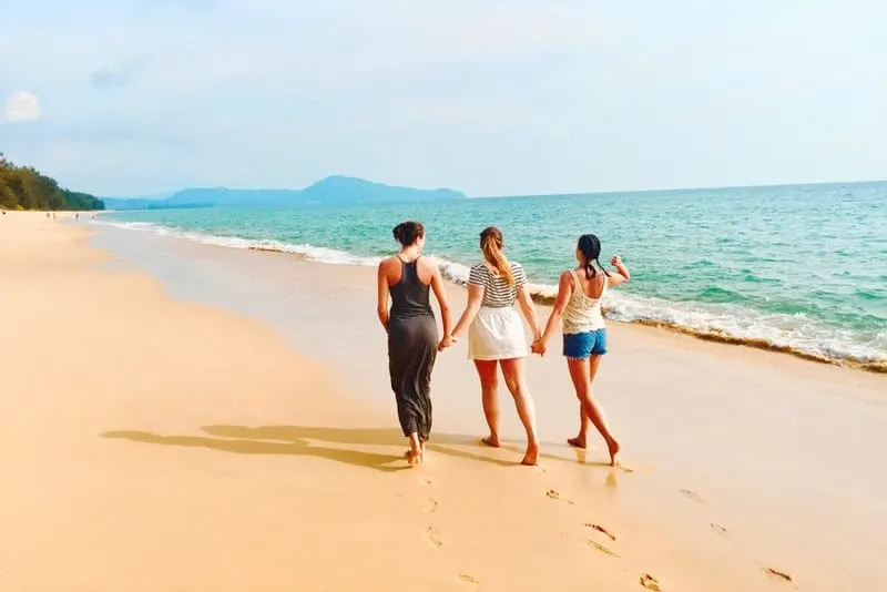 Drei Freunde gehen Händchen haltend am Strand entlang