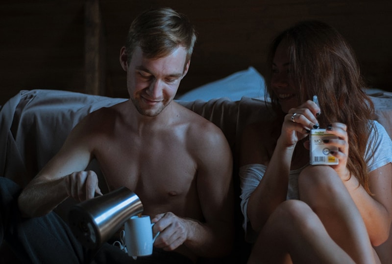 Ein Mann, der Kaffee in die Tasse füllt, sitzt neben einer Frau, die im dunklen Raum einen Saft hält