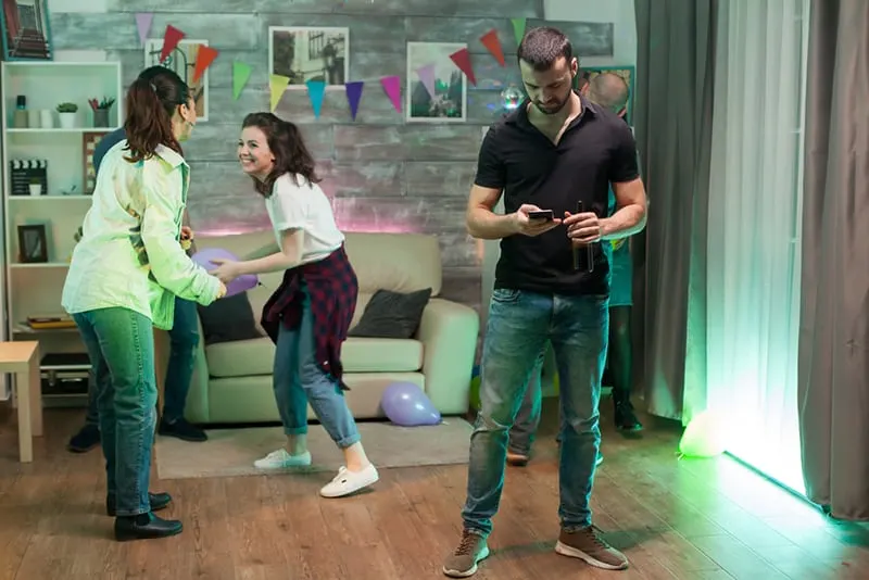 Ein Mann benutzt sein Smartphone auf einer Party, während seine Freunde tanzen