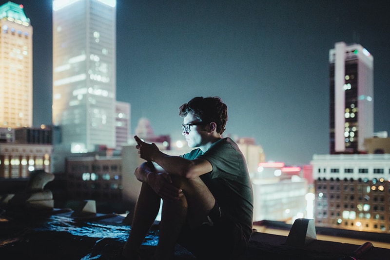 Ein Mann, der nachts oben auf dem Gebäude sitzt und ein Smartphone benutzt