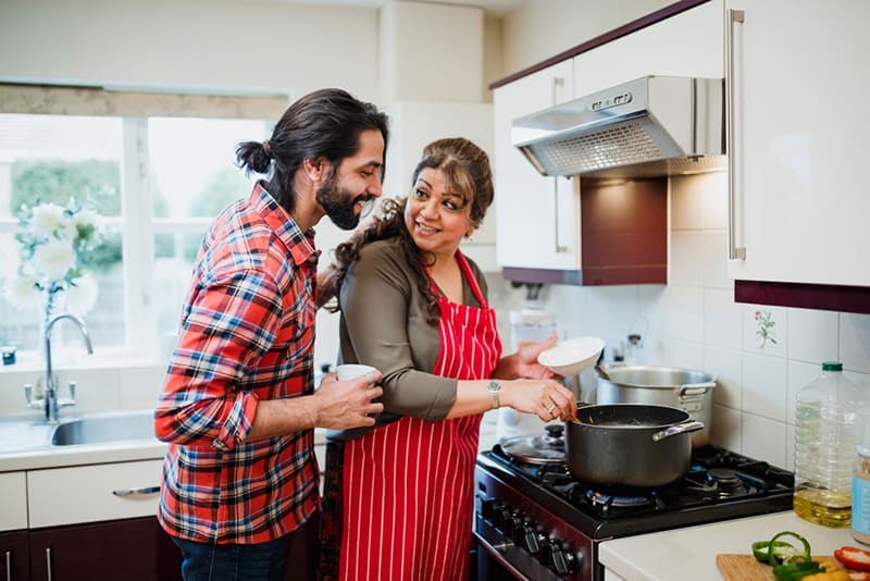 Ein Mann, der seine Mutter beim Zubereiten einer Mahlzeit ansieht, während er neben ihr in der Küche steht