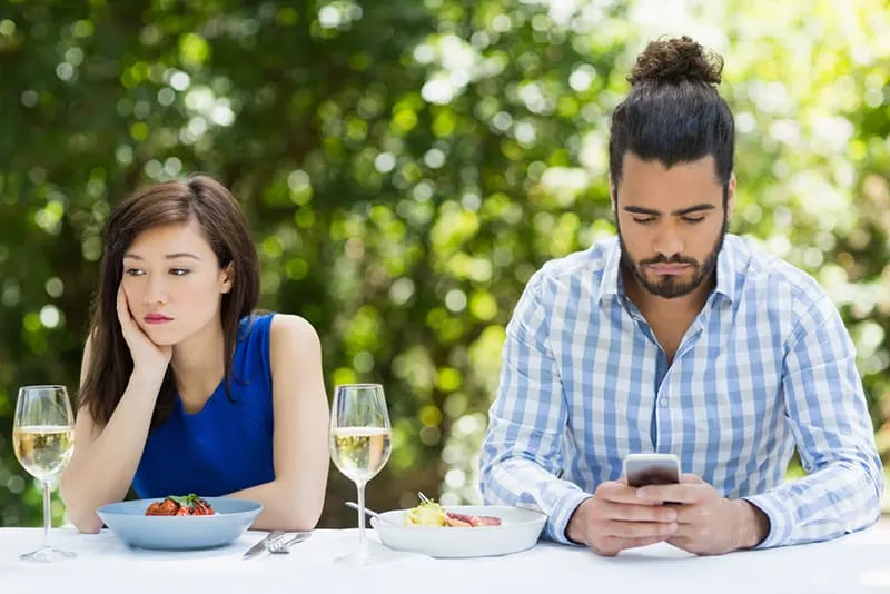 Ein Mann ignoriert die Frau und benutzt ein Mobiltelefon, während er im Restaurant sitzt