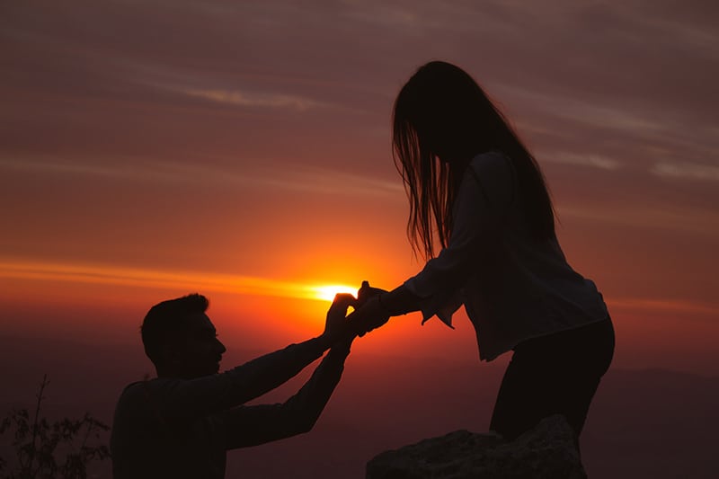 ein Mann vor einer Frau kniet und sie bei Sonnenuntergang vorschlagen