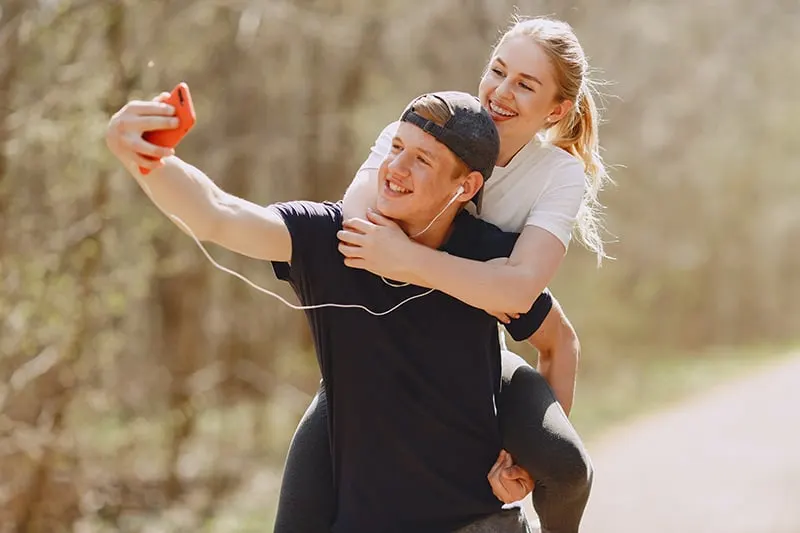 Ein Mann macht ein Selfie von ihm und seiner Freundin, während er sie auf seinem Rücken trägt