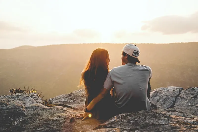 Ein Mann sitzt in der Nähe einer Frau, während er während des Sonnenuntergangs auf dem Felsen sitzt