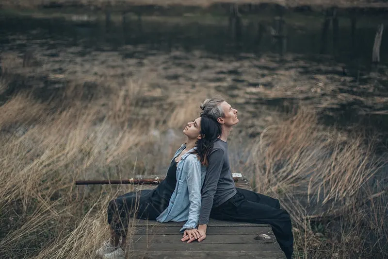 Ein Mann und eine Frau lehnen sich mit dem Rücken aneinander und sitzen auf dem Holzweg