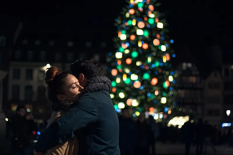 Ein Mann und eine Frau umarmen sich in der Nacht in der Nähe des Weihnachtsbaumes