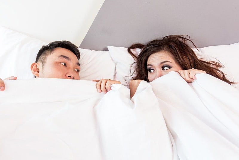 Ein Paar schaut sich an, während es mit weißen Laken im Bett bedeckt