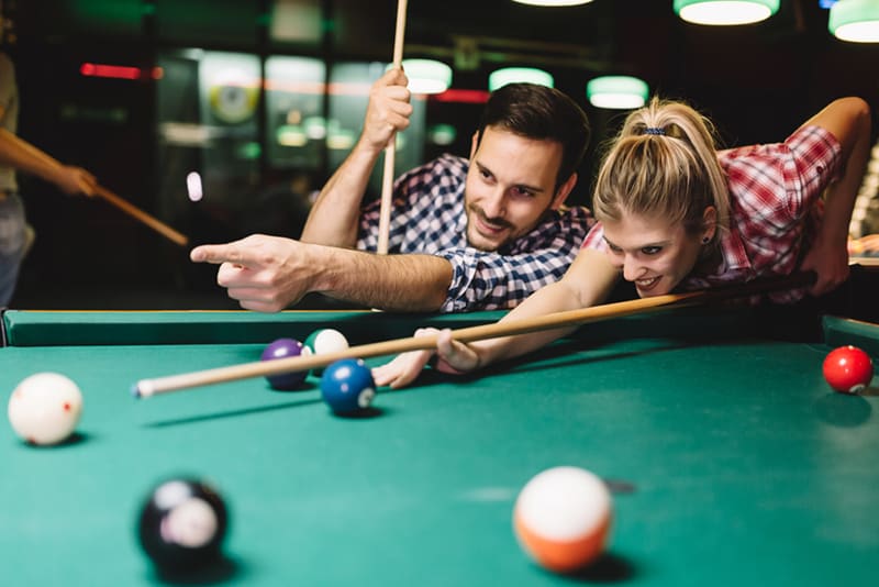 Ein lächelnder Mann, der eine Frau berührt, wie man Snooker spielt, während er zusammen in der Bar rumhängt