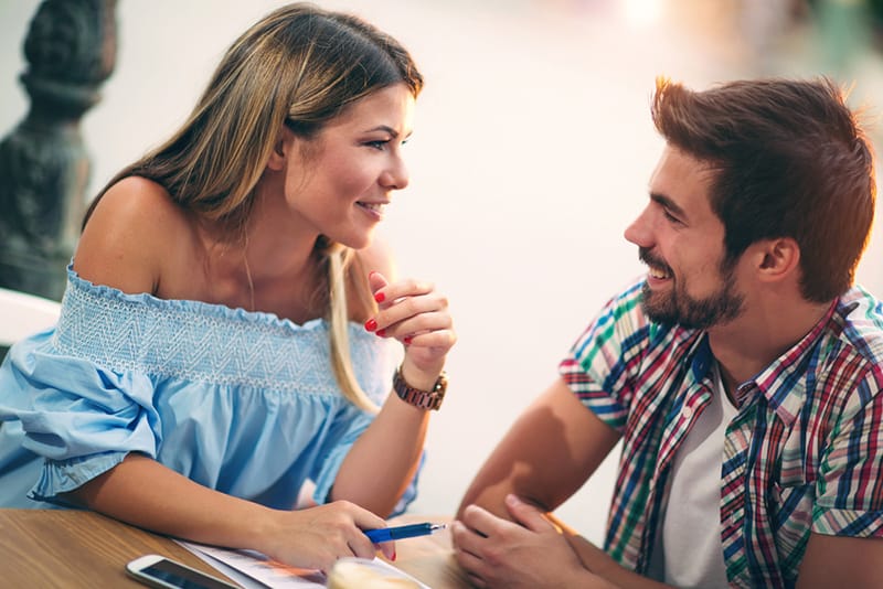 Ein lächelnder Mann und eine Frau unterhalten sich im Café und schauen sich an
