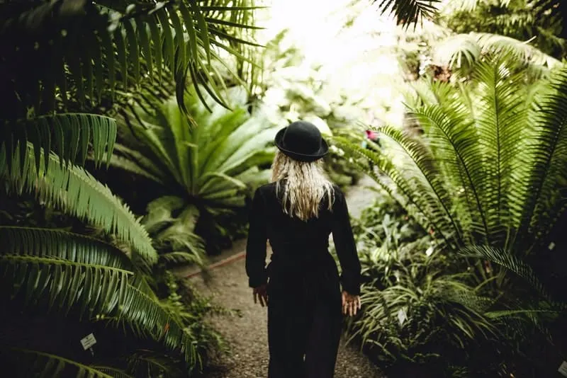 Eine Blondine mit einem schwarzen Hut geht durch den Wald