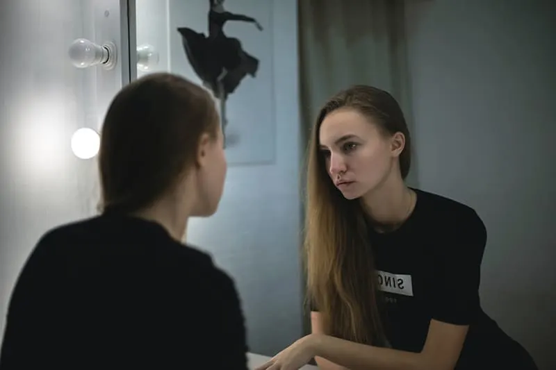 Eine Frau, die sich selbst in den Spiegel schaut und traurig aussieht