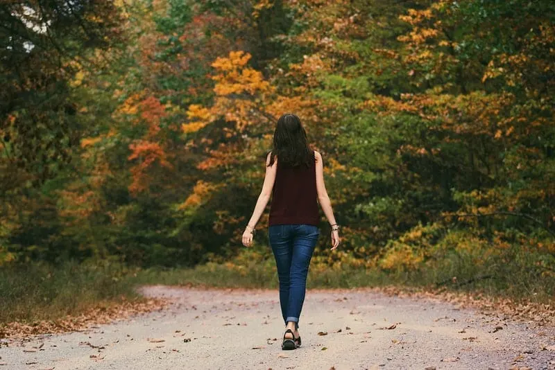 Eine Frau in einem braunen T-Shirt und Jeans geht durch den Wald