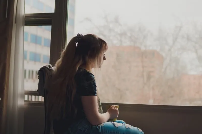 Eine Frau mit Tee in der Hand sitzt am Fenster