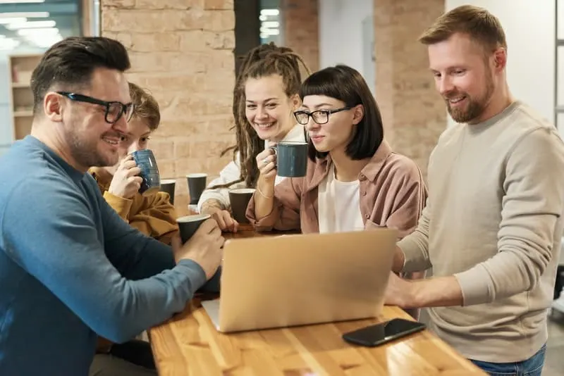 Eine Gruppe von Freunden trinkt Kaffee und schaut sich etwas auf einem Laptop an