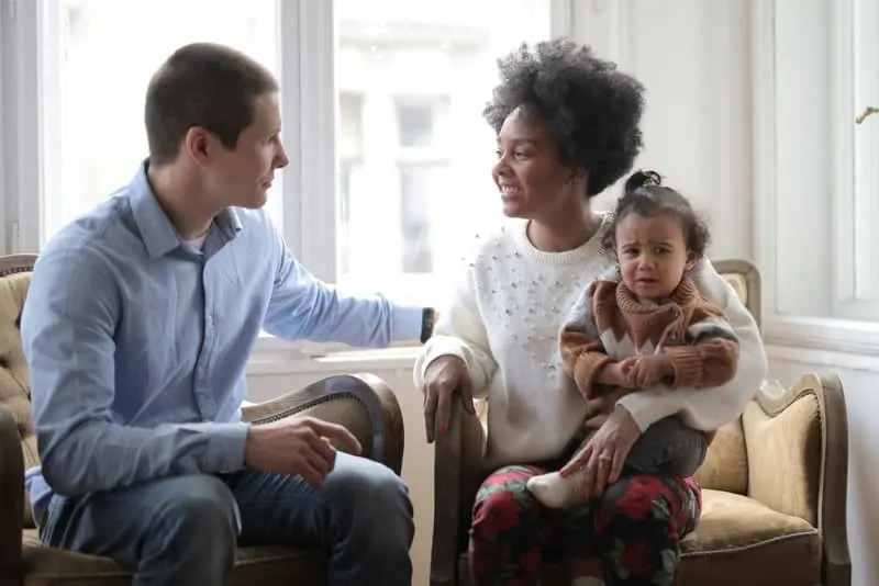 Eine lächelnde Frau mit einem Kind auf dem Schoß spricht mit einem Mann im Haus