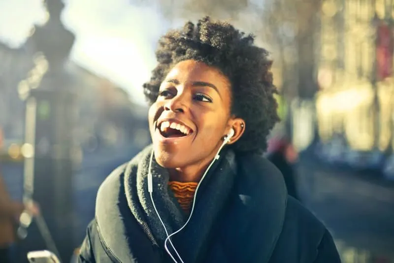 Eine lächelnde schwarze Frau geht die Straße entlang und hört Musik über Kopfhörer