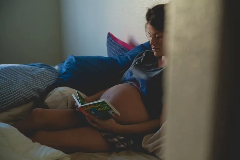 Eine schwangere Frau legt sich hin und liest ein Buch