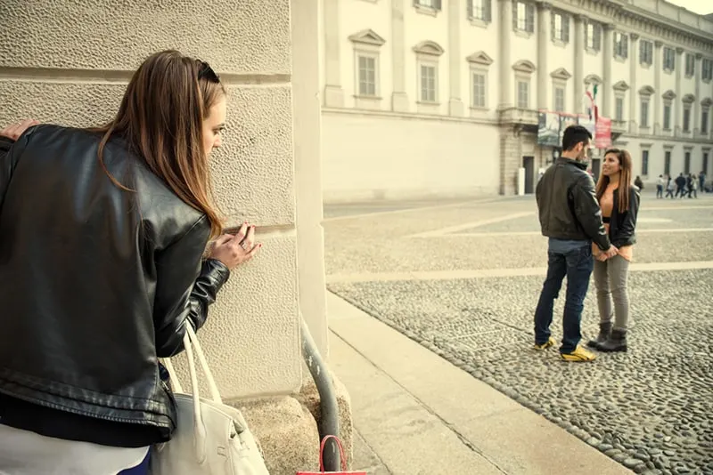 Ex-Freundin spioniert ihren Ex-Freund mit einer anderen Frau aus, während sie sich hinter der Mauer des Gebäudes versteckt