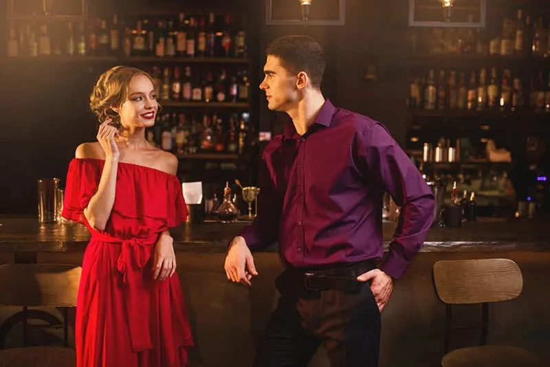 Frau im roten Kleid flirtet mit Mann in der Bar