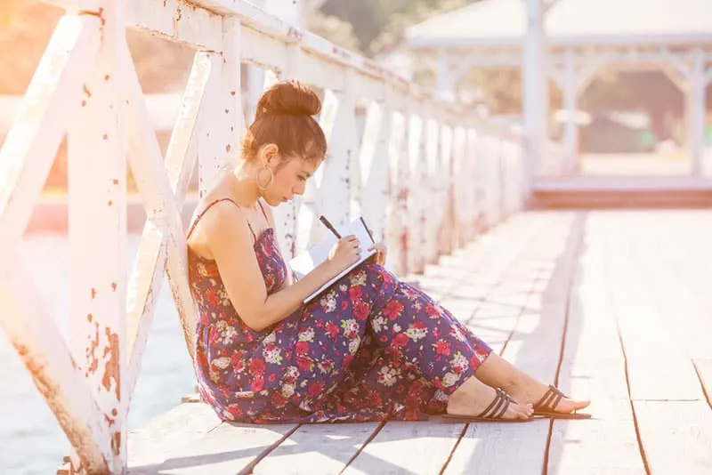 Frau sitzt auf der Brücke und schreibt einen Brief