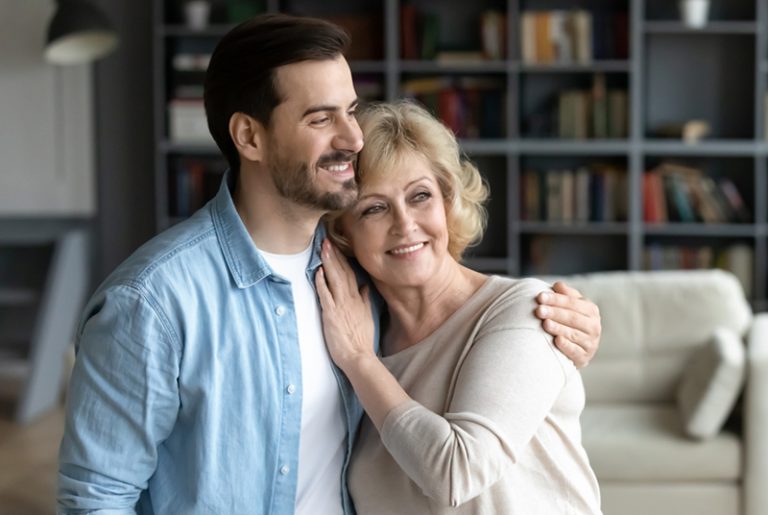 Ein Mann umarmt die Mutter mittleren Alters, während er im Wohnzimmer steht