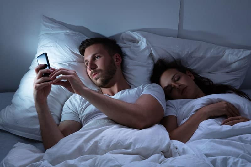 Mann-SMS-während-Frau-schläft