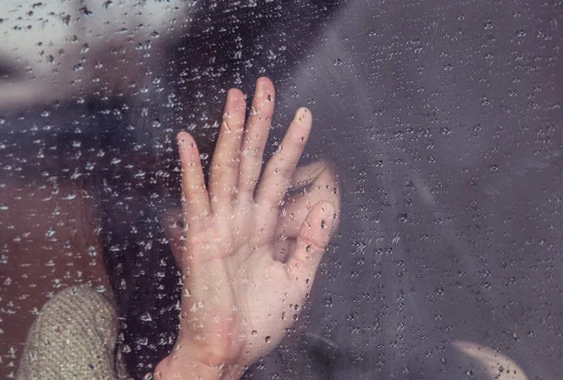 ein junges Mädchen, das am regnerischen Fenster weint