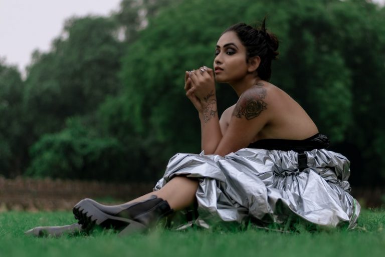 Eine Brünette in Stiefeln und ein graues Kleid sitzt im Gras