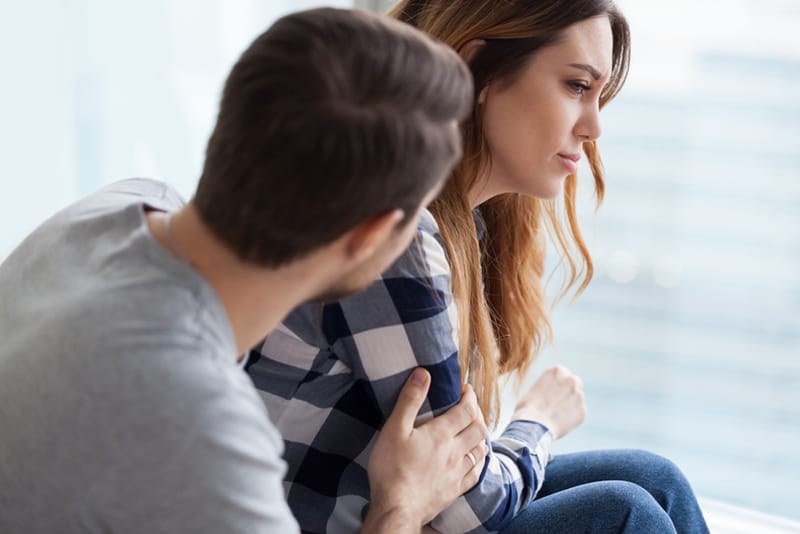 Ein Mann, der eine beleidigte Frau tröstet, die sie von hinten streichelt und umarmt