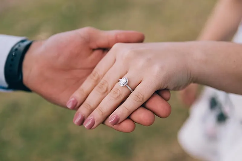 Ein Mann hält die Hand einer Frau mit einem Verlobungsring am Finger