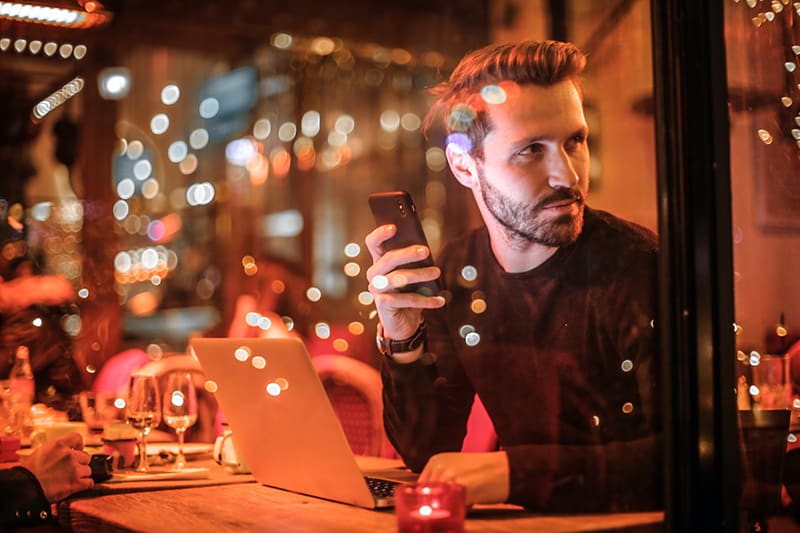 ein Mann, der ein Smartphone hält, während er durch das Fenster schaut, während er im Café sitzt