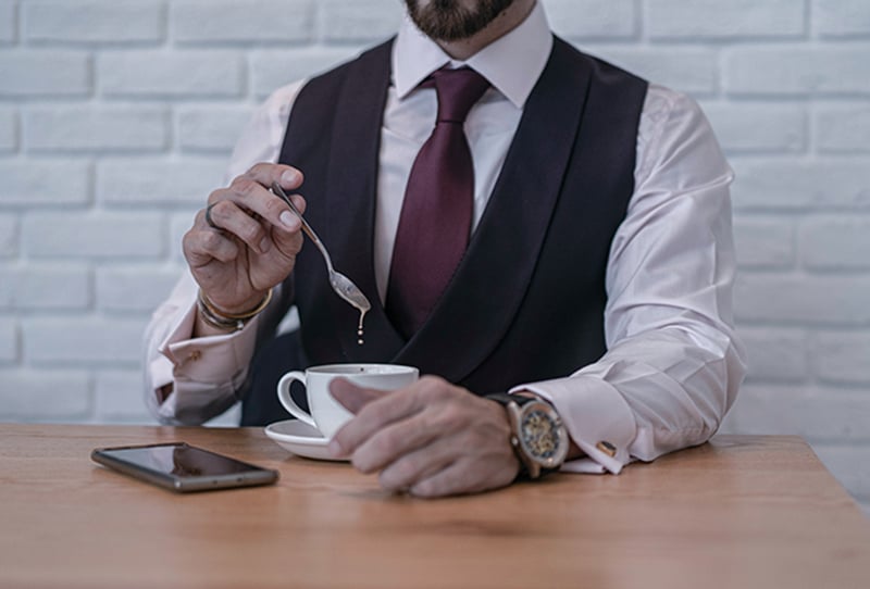ein Mann, der einen Teelöffel hält, während er einen Kaffee auf dem Tisch in der Nähe des Smartphones mischt