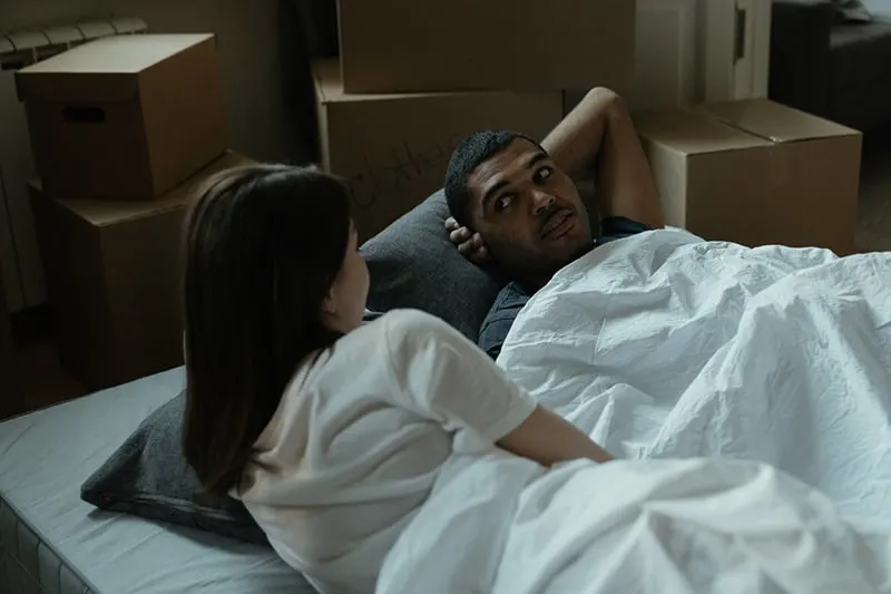 Ein Mann schaut zu seiner Freundin, während er auf dem Bett liegt