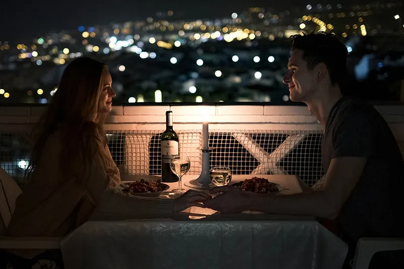 ein Paar Händchen haltend beim romantischen Abendessen auf dem Balkon