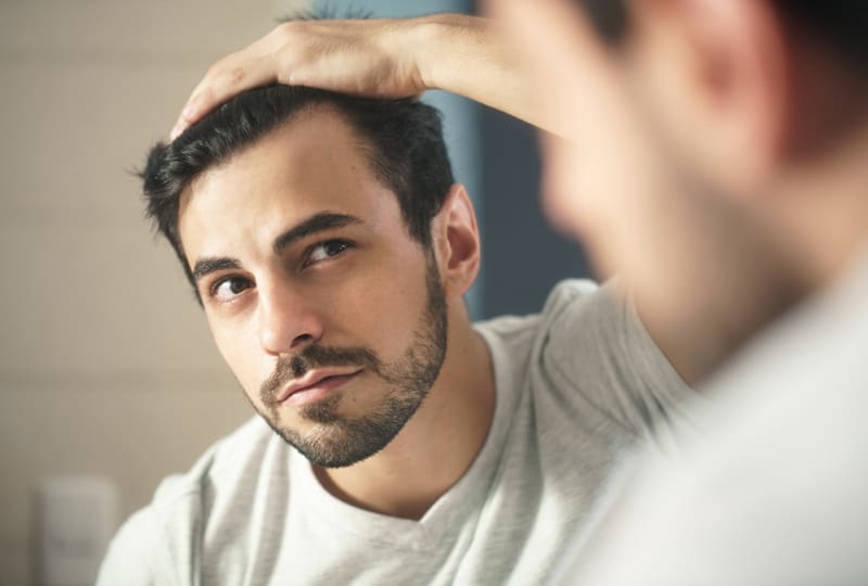 Ein bärtiger Mann, der sich im Spiegel nach den ersten grauen Haaren umschaut