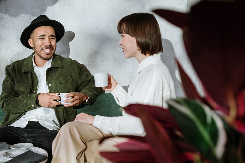 Ein lächelnder Mann, der verwirrt aussieht und mit einer Frau spricht, während er zusammen im Café sitzt