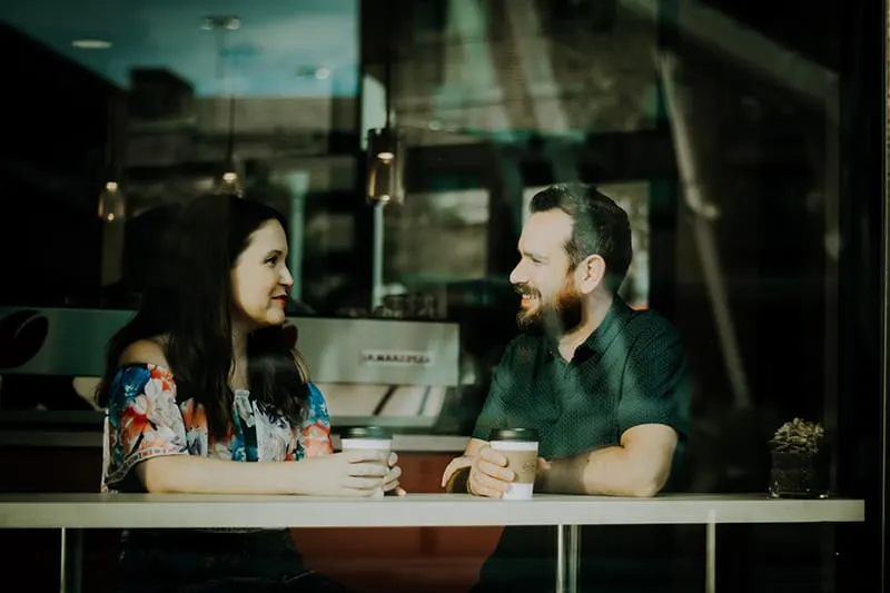 Ein lächelnder Mann, der zu einer Frau schaut, während er zusammen im Café sitzt und sich unwohl fühlt