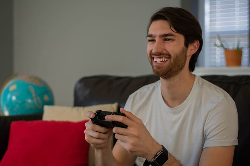 ein lächelnder Mann, der Videospiele spielt, während er auf der Couch sitzt