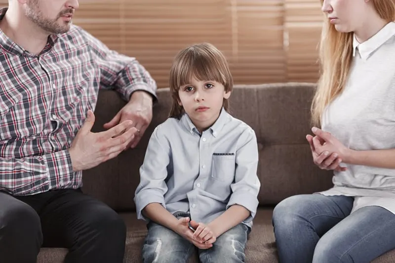 ein trauriges Kind, das zwischen seinen Eltern sitzt, während sie mit ihm sprechen