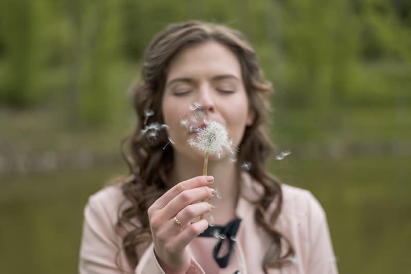 eine Frau, die Löwenzahnblume mit geschlossenen Augen bläst