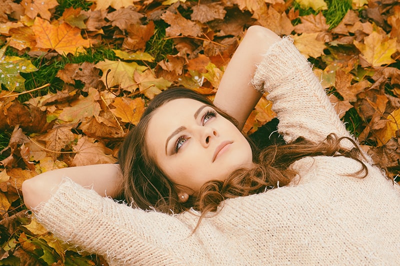 eine Frau, die auf getrockneten Blättern liegt und aufschaut