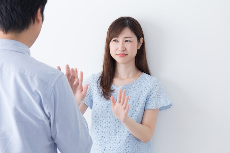 eine Frau, die einen Mann mit ihren Handflächen vor sich ablehnt und sich unwohl fühlt