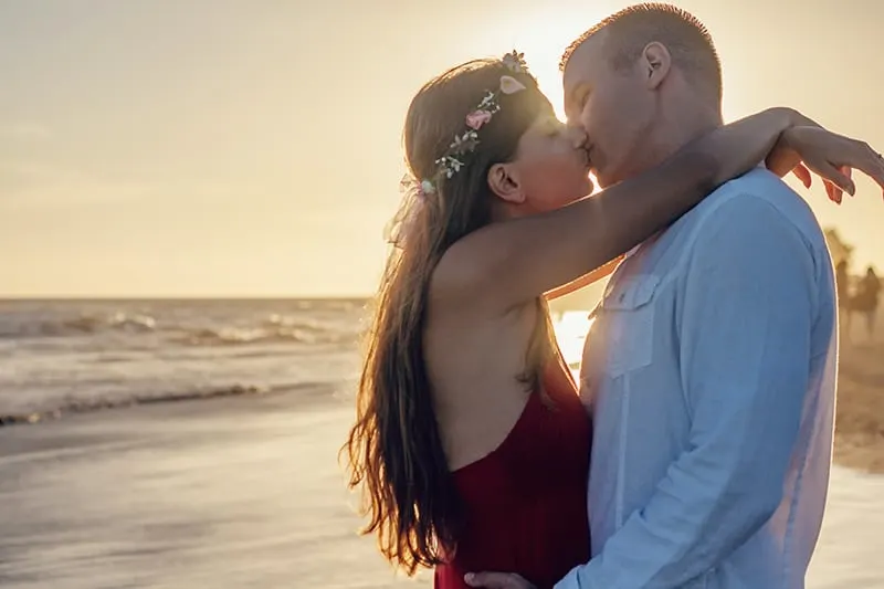 eine Frau, die einen Mann umarmt, während sie sich mit ihm küsst, während sie am Strand steht