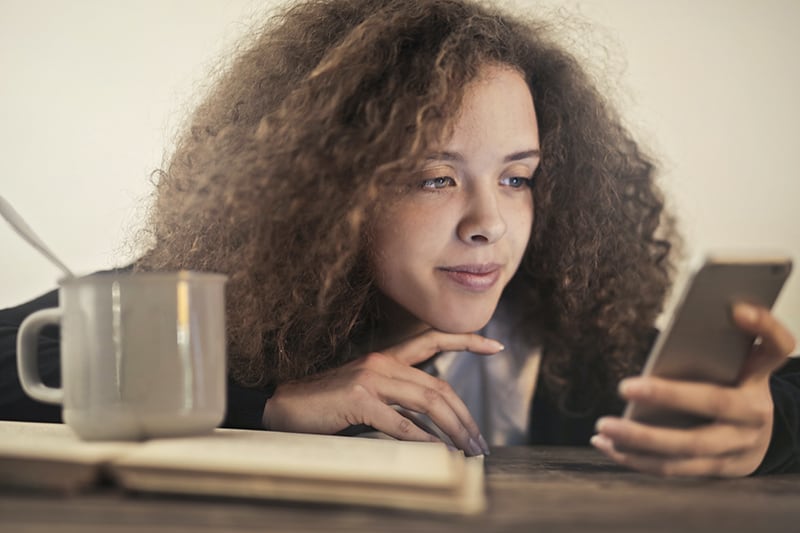 eine Frau, die ihr Kinn berührt, während sie auf das Smartphone schaut und überrascht aussieht