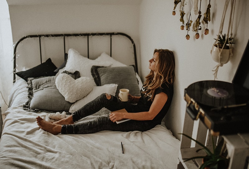 eine Frau, die sich an die Wand lehnt, während sie auf dem Bett sitzt und nachdenklich aussieht