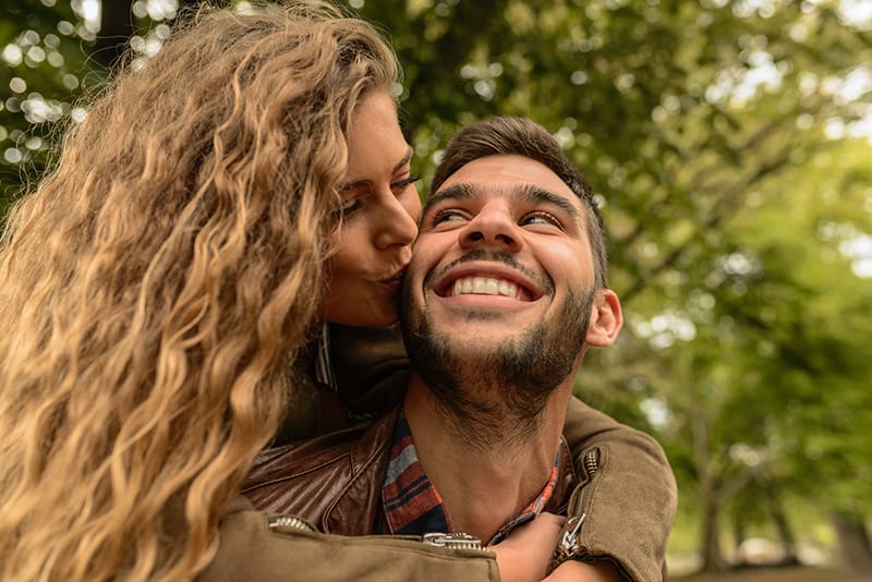 Eine Frau küsste ihren Freund von hinten auf die Wange und umarmte ihn
