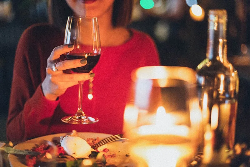 eine Frau, die beim Abendessen ein Glas Wein in der Hand hält