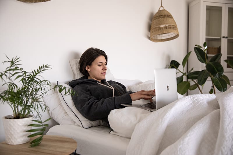 eine Frau, die einen Laptop benutzt, während sie auf dem Bett liegt